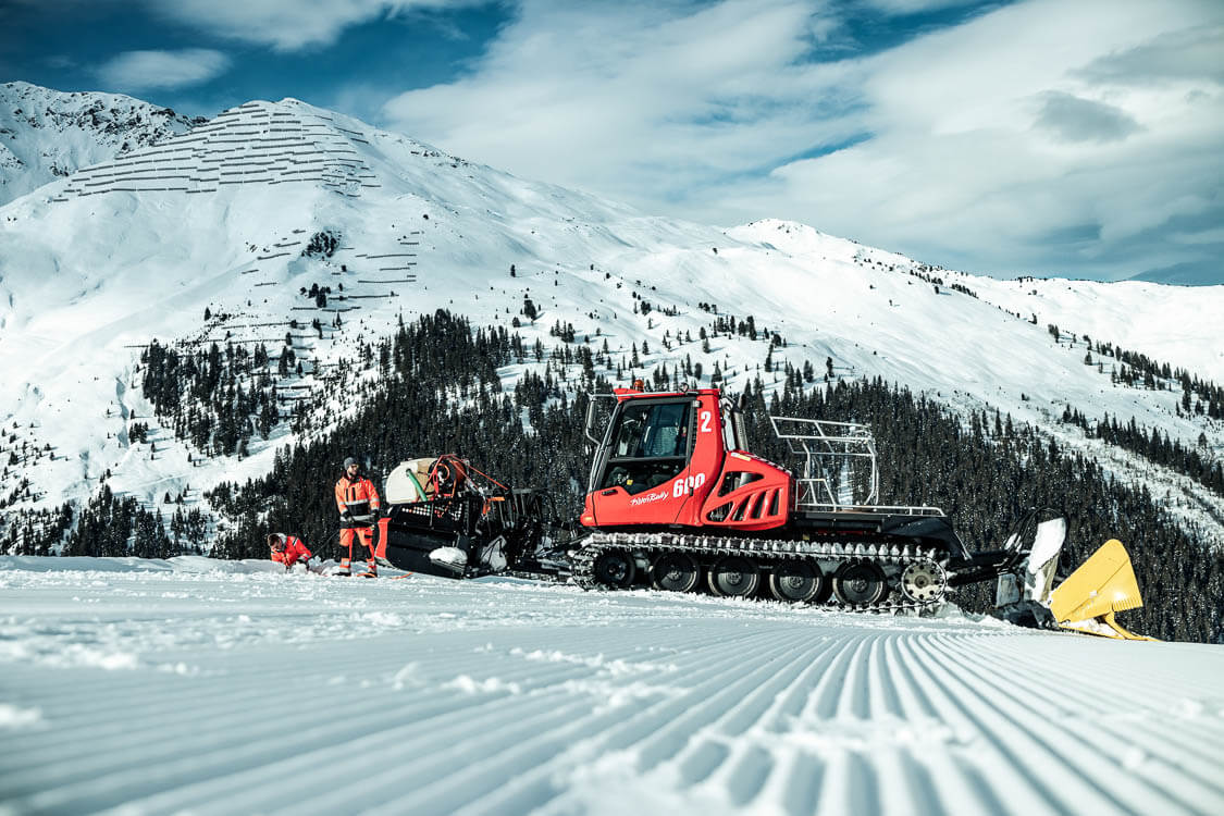 Zwei DAWI Mitarbeiter neben einer Pistenraupe transportieren Gerätschaften für Kanalreinigung am Berg